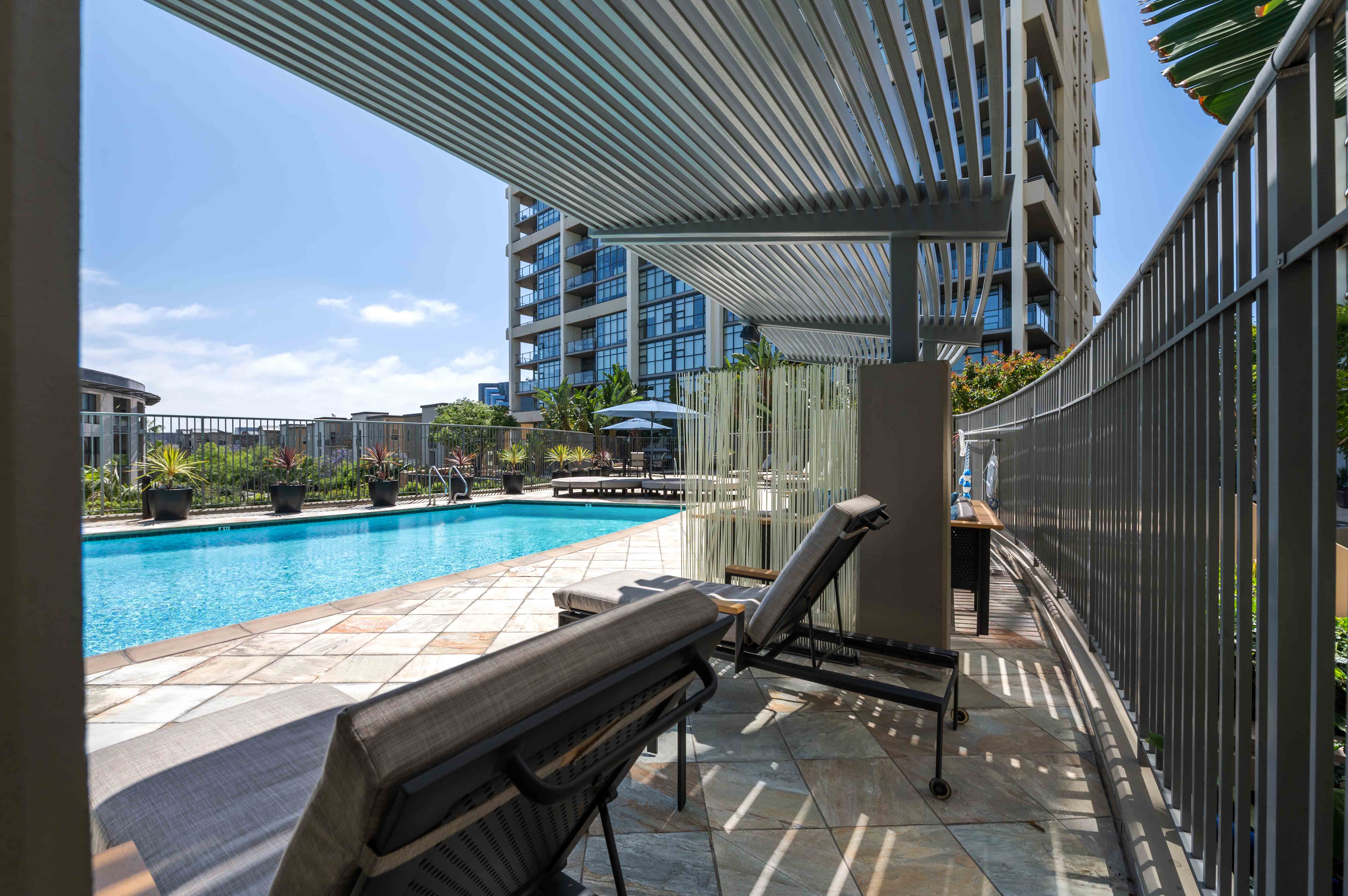 Irvine, CA, Apartments for Rent - Astoria at Central Park West - Gated Pool with Lounge Chairs, Umbrellas, and Potted Plants.